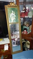 Full view of antique mirror showing wood frame, portrait, and mirror portion, with some reflected objects around.