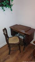 Side view of the antique Singer sewing machine cabinet with treadle base and wooden chair with caned seat