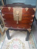 Front view of the Chinese chest on stand, showing wood grain finish and brass hardware including front lock and corner brackets.