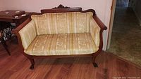 Front view of antique Victorian Eastlake wood settee with light gold and cream patterned flocked velvet upholstery, claw feet visible on front.