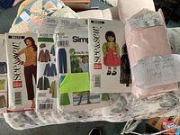 Photo showing several sewing patterns for women and one doll dress pattern, plus a packet of pink fabric for dressmaking.