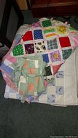 Overview of two patchwork quilts and a patchwork apron stacked together on floor.