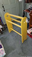 Photo showing front and side of yellow distressed wood quilt rack with curved ends and heart cutouts