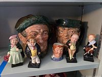 Full lot of 4 miniature figurines and 3 large character jugs displayed on shelf