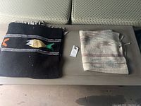 Two woven scatter rugs placed folded on light furniture, showing one black rug with fish designs and one lighter colored rug.