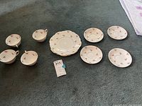 Photo showing five bone china tea cups and five matching saucers arranged on carpet. Cups and saucers have pink rose floral pattern.