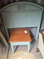 Matching wood nightstand with natural wood finish top and duck egg blue painted legs, in front of the headboard.