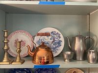 Display of the brass candlesticks, copper kettle, and International Pewter coffee set along with willow and Wedgwood plates on shelf.