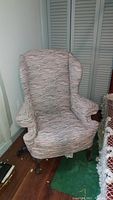 Side-angle photo showing wingback chair with claw and ball feet, reupholstered multicolored fabric upholstery and visible wear.