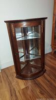 Front view of vintage wooden corner display cabinet showing rounded glass door and wood carving details.