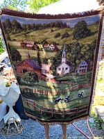 Full view of the woven tapestry showing complete rural countryside with buildings, trees, fences, cattle, and hills under sunlight.
