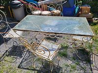 Front and side view of antique bent iron outdoor table with clear plate glass top and four matching bent iron chairs with woven metal seats around the table.