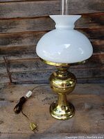 Full view of weighted brass lamp base with glass chimney and white glass shade, showing electrical cord and switch.