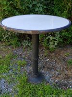 Full view of antique white enameled round pub table with blue band and cast iron base on outdoor gravel and grass surface