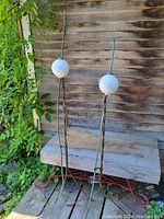 Pair of antique lightning rods standing vertically showing twisted copper rods topped with white milk glass balls against a wooden background.
