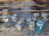 Photo showing all nine antique glass jars with various lids arranged on rustic wooden surface