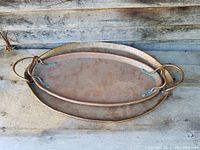Photo showing two oval hand hammered copper serving trays stacked, with visible patina and handles attached with rivets.
