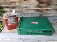 Closed green Coleman camp stove and red metal fuel can on weathered wood surface.