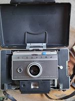 Polaroid Land Camera Auto 100 inside original hard case, showing camera front and lens details