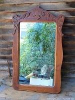 Front view of the oak framed mirror showing carved wooden top and reflective glass surface with outdoor background reflections.