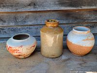Three early pottery items: one shellac crock and two native open bowls arranged side by side on a wooden surface with a weathered wood background.