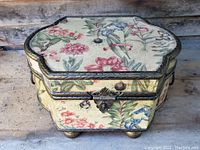 Closed floral fabric covered jewelry box with ornate metal trim and small feet.