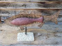 Full view of hand made metal fish sculpture showing the design, metal rod, and stone base.