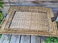 Top-down photo of large rectangular wicker serving tray showing woven wicker pattern and handles.