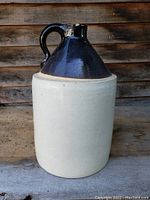 Photo of front angle showing the full body and handle of the vintage whiskey crock jug with cream base and dark upper glaze.