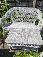 White wicker love seat and square table placed outdoors. The set shows signs of wear, discoloration, and dirt.
