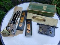 Old Yale lockset pieces arranged on a white circular table, showing lock mechanism, handles on backplates, escutcheon plates, a latch, various small parts, and the original green and gold Yale box.