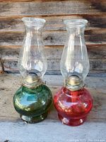 Pair of oil lamps with round glass bases, one red and one green, with clear glass chimneys and brass burners.