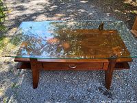Front angled view of the walnut coffee table with beveled glass top showing drawer open from both sides and tapered wooden legs.