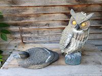 Both rubber decoys, owl standing and duck lying down against wooden background