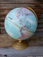 Full view of vintage rotating globe with blue oceans and multi-colored continents, mounted on a gold-toned base.