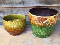 Two vintage jardiniere pots side by side on wooden surface, one larger with distinctive relief patterns and one smaller with distinctive scalloped edge.