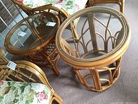 Two bamboo side tables with round glass tops and natural bamboo open-frame bases on carpeted floor.