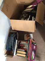 Boxes filled with various paperback books including bird books, Lancaster County history books, and fiction, as well as an umbrella partly visible inside one box.