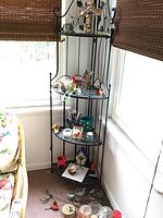 Metal corner rack with bird figurines, candles, and decorative items placed next to a window.