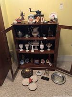 Photo showing the full wooden cabinet filled with assorted milk glass pieces, teacups, a vintage coffee grinder, a ceramic pitcher, and decorative plates on and around the cabinet.