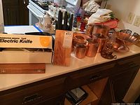 Wide shot showing electric knife box, wooden case, knife block and copper items on countertop