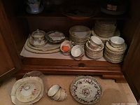 Image showing stacks of cups, saucers, bread plates, soup bowls, lidded bowl, and other pieces in a wooden cabinet storage unit
