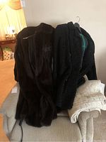 Two fur coats on a chair: one brown mink and one black curly lamb coat.