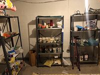 Three metal shelving racks, each with four shelves and black metal framing, shown in basement setting with various items on shelves that are excluded from sale.