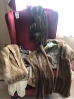 Two mink stoles draped on a red chair, showing both front and lining of the fur pieces.