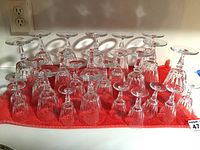 Full overview of all three sets of Princess House glasses arranged on a red cloth showing 24 glasses in total upside down.