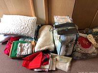 Photo showing quilt, pillows, red and green cloth napkins/tablecloths, and packaged yarn or textiles on a surface
