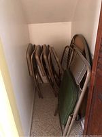 Cluster of folding chairs including four matching brown padded chairs and one green padded chair, stacked closely in a corner.