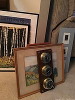 Overview of multiple framed wall art pieces including landscape, birch tree prints and a vintage weather station with three brass dials mounted on wood.