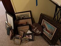 Various wall art and frames stacked against a wall on carpet floor showing different sizes and styles including plaques and framed photograph